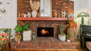A brick fireplace with a mirror above it, surrounded by various decorative items and plants.