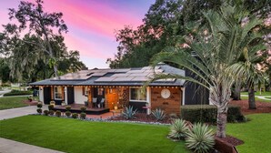 A modern house with a well-maintained lawn, a porch with outdoor seating, and a large clock on the front wall.