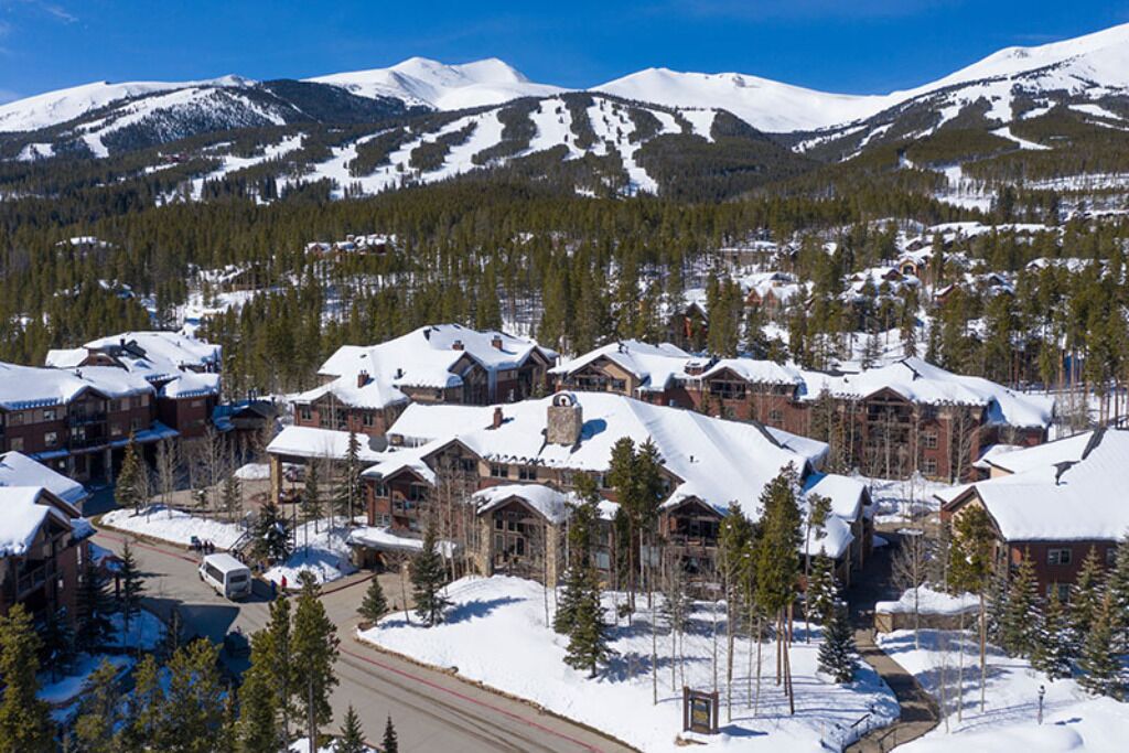 A snow-covered lodge with multiple buildings, surrounded by trees and mountains.