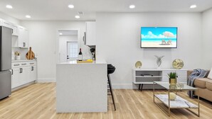 Une cuisine moderne avec des meubles blancs, un îlot central et un coin repas doté d’une table en verre.