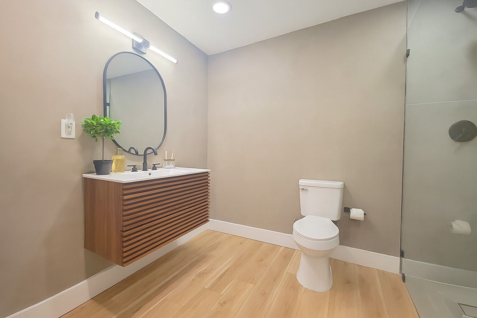 A modern bathroom with a wooden vanity, a white toilet, and a glass shower enclosure.