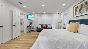 Une chambre d’hôtel moderne avec un grand lit, un téléviseur fixé au mur, un bureau avec une chaise et une vue sur la plage à travers les rideaux.