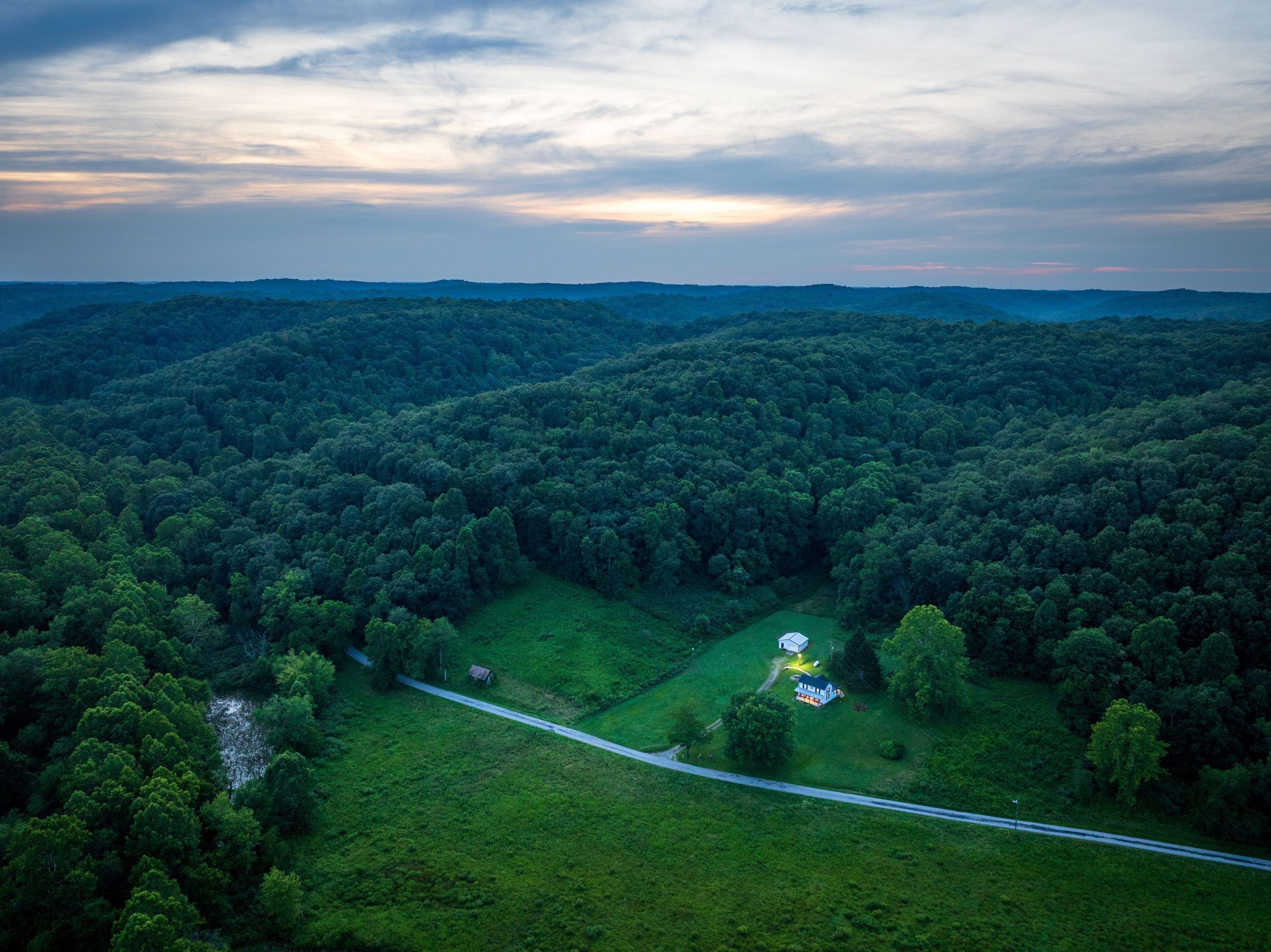 An aerial view of a forested area with a road leading to a small house surrounded by greenery.