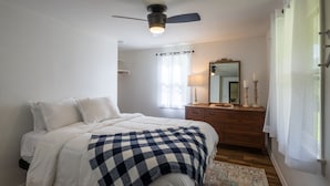 Un dormitorio con cama, ventilador de techo, cómoda, espejo y ventana con cortinas.