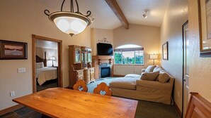 A cozy room with a wooden dining table, a sofa, a television, and a fireplace. - 3057 | Alpine King Villa | Near Wasatch SP + Pool (Midway)