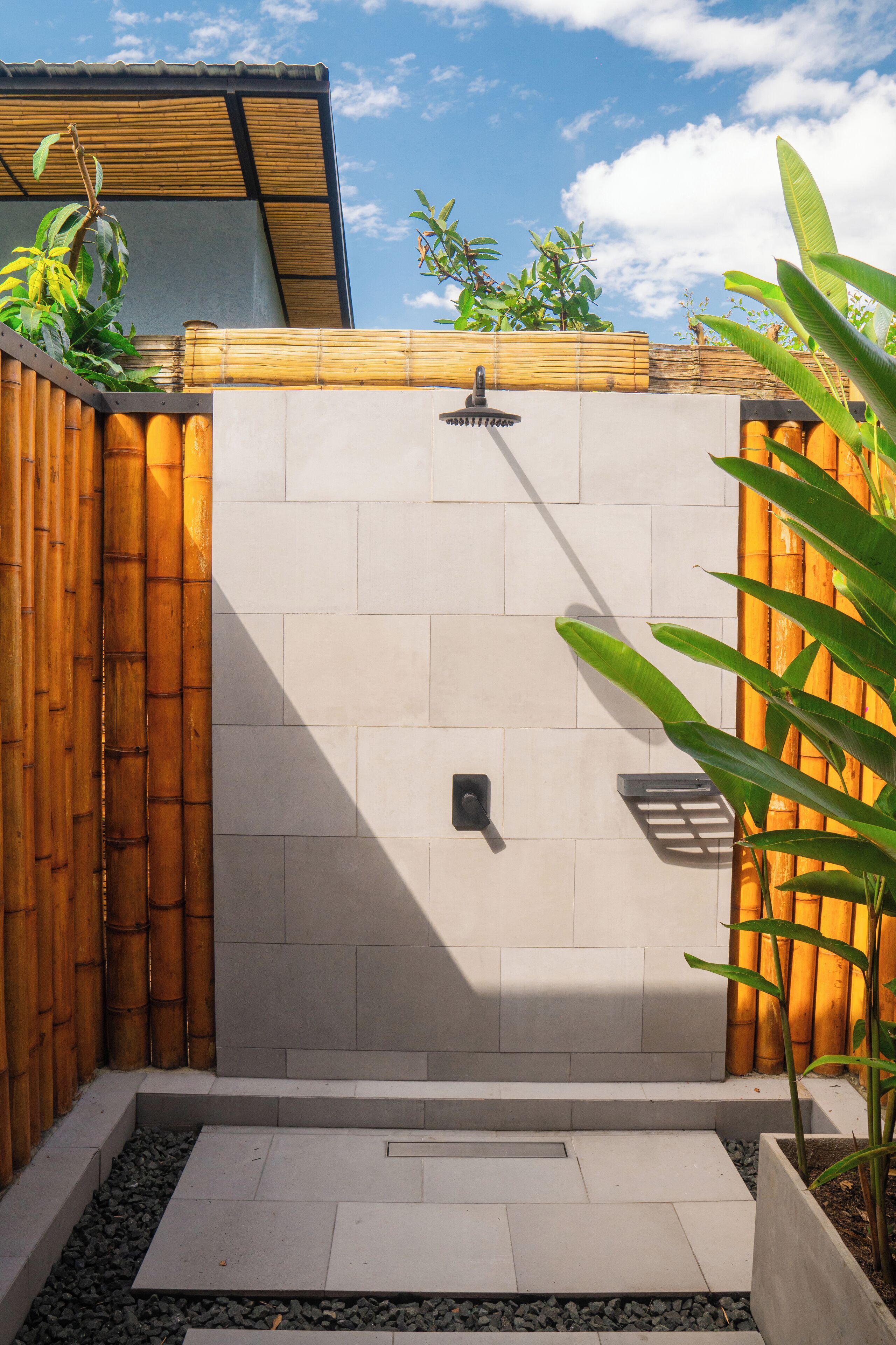 A modern outdoor shower area with a bamboo fence, tiled walls, and a small planter with greenery.