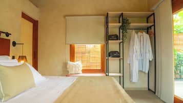 Une chambre d’hôtel avec un lit, une table de chevet, une fenêtre avec des stores, une armoire et une plante.