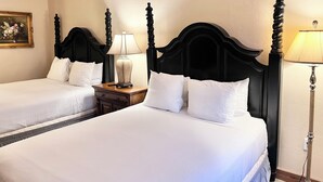 Habitación de hotel con dos camas, cada una con cabecero de madera, una mesita de noche con lámpara y un cuadro de flores enmarcado en la pared.