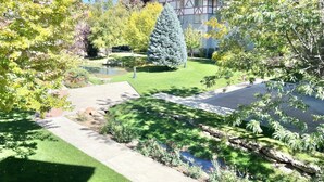 Un jardin bien entretenu, agrémenté d’un étang, de différentes espèces d’arbres et d’un bâtiment visible au loin.