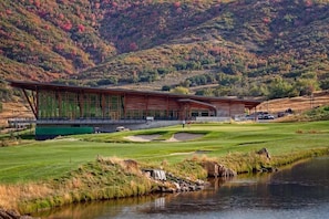 A modern building with a large glass facade, situated next to a golf course and a body of water.