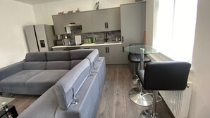 A modern living room with a grey sectional sofa, a glass-top coffee table, and a black bar stool.