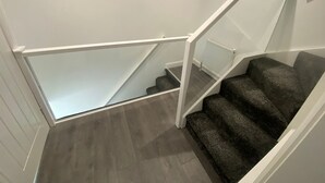 A staircase with a glass railing, carpeted steps, and a white wall.