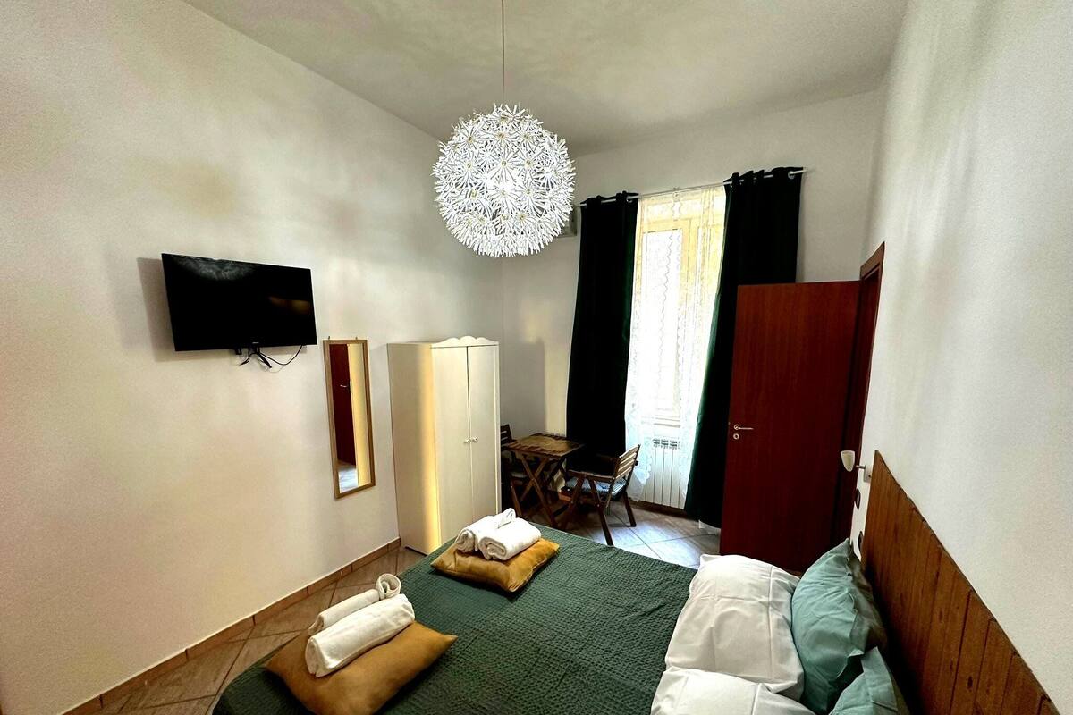 A hotel room with a bed, a television, a wardrobe, a mirror, and a dining area with a table and chairs.