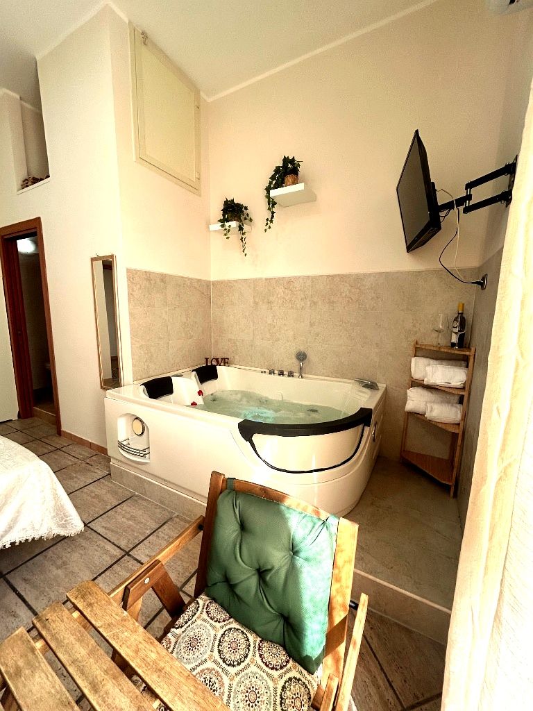 Un baño con bañera, una silla de madera con cojín, un estante con toallas y un televisor montado en la pared.