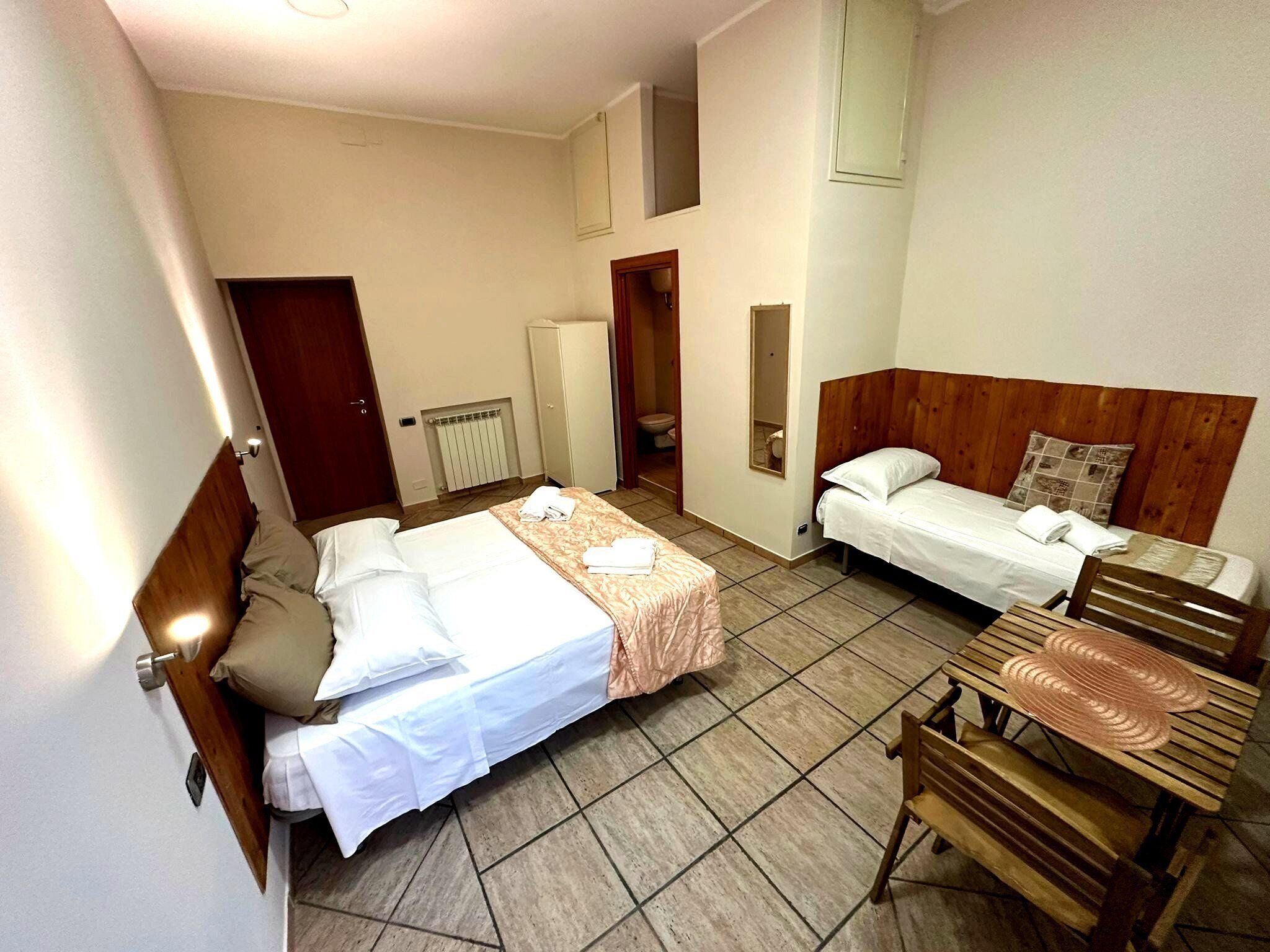 Hotellihuone, jossa on kaksi sänkyä, puinen penkki, patteri ja ovi.