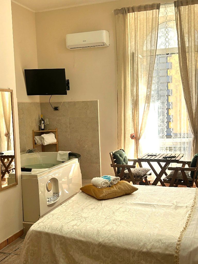 Habitació d'hotel amb un llit, una televisió, una finestra amb cortines, una taula petita amb cadires i un aire condicionat fixat a la paret.