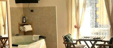 A hotel room with a bed, a television, a window with curtains, a small table with chairs, and a wall-mounted air conditioner.