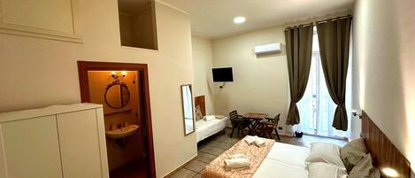A hotel room with a bed, a desk, a chair, a small bathroom with a sink, and a TV mounted on the wall.