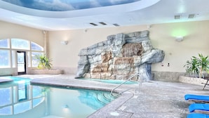 Una piscina con un muro de piedra y sillas de descanso azules.