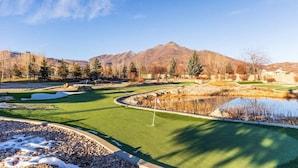 A golf course with a flag, a pond, and mountains in the background.