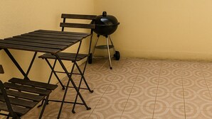 Un patio exterior con una mesa y sillas, una parrilla y luces colgantes frente a una pared amarilla.