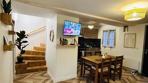 Una sala moderna con suelo de espiga, comedor con muebles de madera, cocina con encimera negra y televisor montado en la pared.