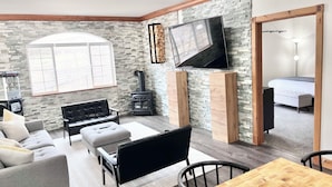 A living room with a stone wall, a fireplace, a television, a sofa, a coffee table, and a dining area. - 2037/39 | Elevated 2BR Villa | Near Park City Ski (Midway)