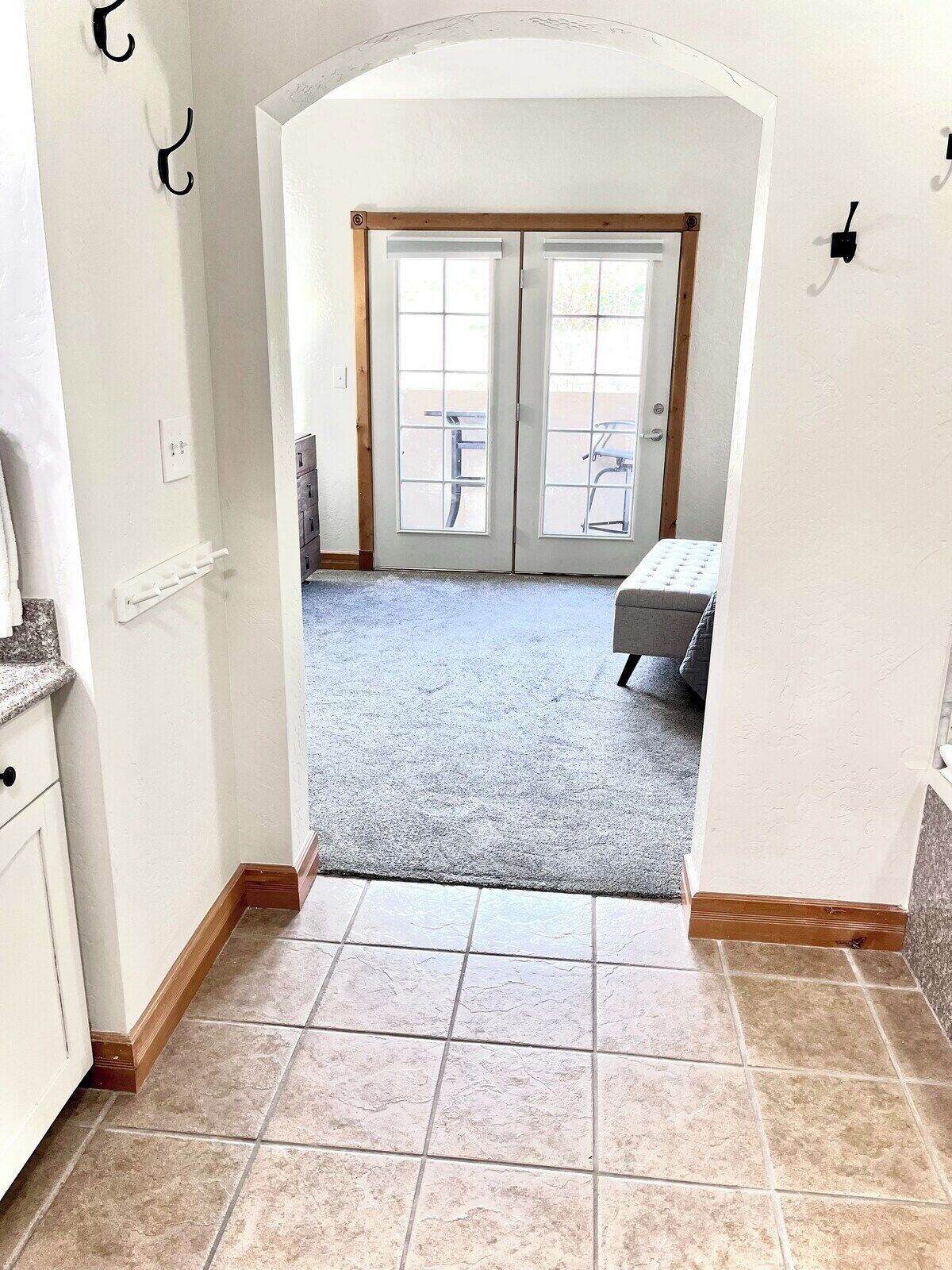 A hallway leading to a room with a double door, a bench, and a tiled floor.