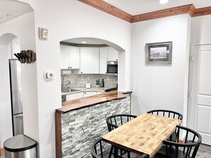 Une cuisine compacte avec des meubles blancs, un îlot central en bois et un pare-feu en pierre.
