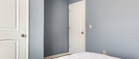 A bedroom with two white doors, a white bedspread, and light blue walls.