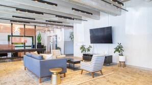 A modern living room with a sofa, armchair, and coffee table, a flat-screen TV mounted on the wall, and a large window providing natural light. - East Side Studio Apt - Near Brady St and Fiserv with Balcony (Milwaukee)