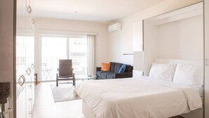 A hotel room with a large bed, a seating area with a chair and sofa, and a balcony with a view of the city. - East Side Studio Apt - Near Brady St and Fiserv with Balcony (Milwaukee)