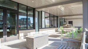 An outdoor seating area with tables and chairs, a stone bench, and large windows offering views of the city. - East Side Studio Apt - Near Brady St and Fiserv with Balcony (Milwaukee)