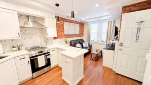 A modern kitchen with white cabinetry, a brick accent wall, and a central island. - The Shoreline Studio - Perfect AC Getaway! (Atlantic City)