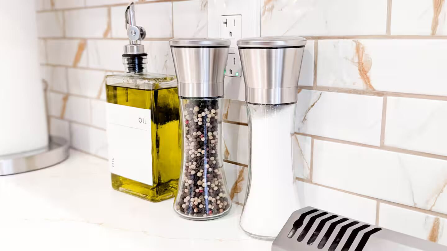 A kitchen counter with a bottle of oil, a pepper grinder, and a salt shaker.