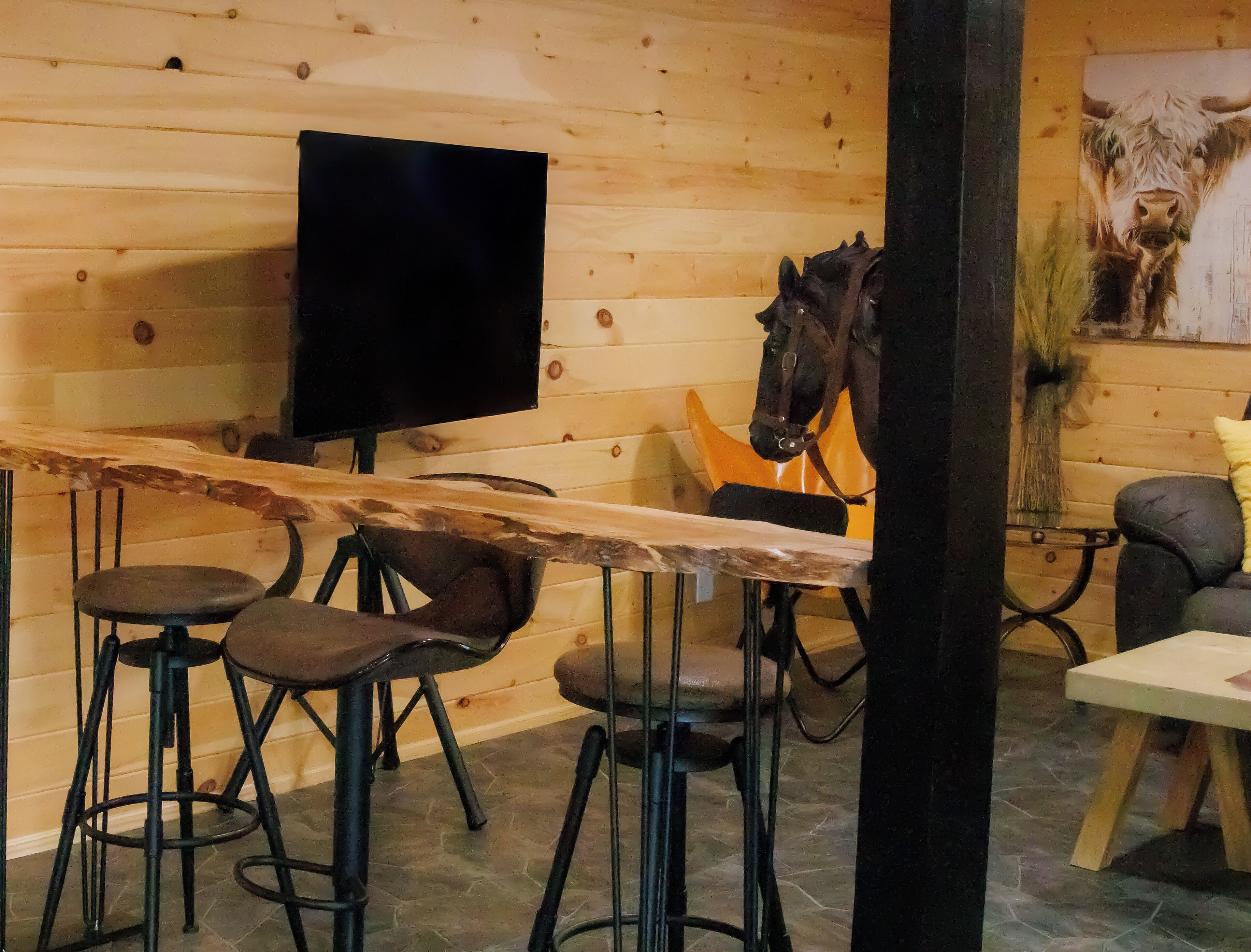 A wooden interior with a bar area, stools, a television, and a horse sculpture.