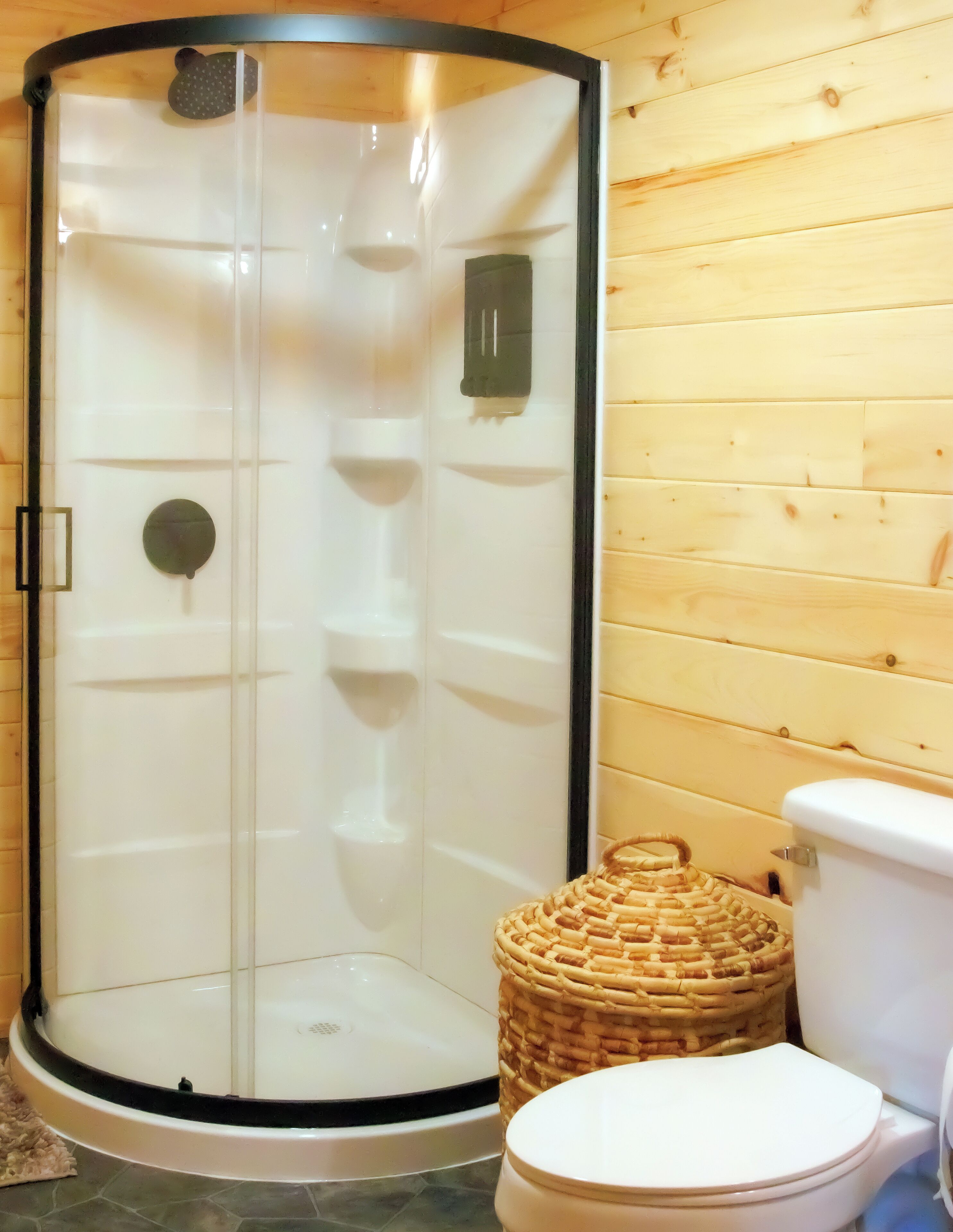 Box doccia con porta in vetro, un water e un cesto di vimini.