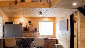 A compact kitchen with wooden walls, a window, a sink, and bar stools.