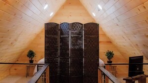 A wooden interior with a sloped ceiling, a black decorative partition, and two potted plants.