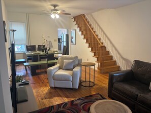 A spacious living area with a wooden staircase, a dining table with chairs, a leather sofa, and a small round table. - Here's a wonderful 3-bedroom brickhouse with AC in charming Wilmington, Delaware (Wilmington)