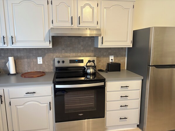 A kitchen with white cabinetry, a stainless steel refrigerator, a black stove, and a toaster. - Here's a wonderful 3-bedroom brickhouse with AC in charming Wilmington, Delaware (Wilmington)