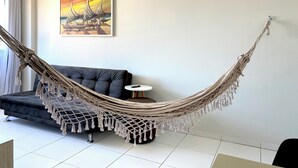 A hammock in a living room with a sofa and a painting on the wall. - 02 QUARTOS próximo a PRAIA de PAJUÇARA (Maceió)