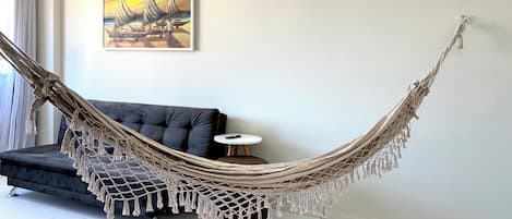 A hammock in a living room with a sofa and a painting on the wall.