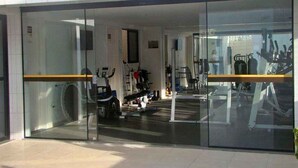 A modern building entrance with glass doors, a visible gym area with exercise equipment, and a sign indicating a business or office space. - 02 QUARTOS próximo a PRAIA de PAJUÇARA (Maceió)