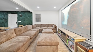 A modern living room with a sectional sofa, a large flat-screen TV, and a bookshelf. - Spacious 5BR Athens Home | Massage Chairs & Fire Pit | Sleeps 12 | Near UGA (Athens)