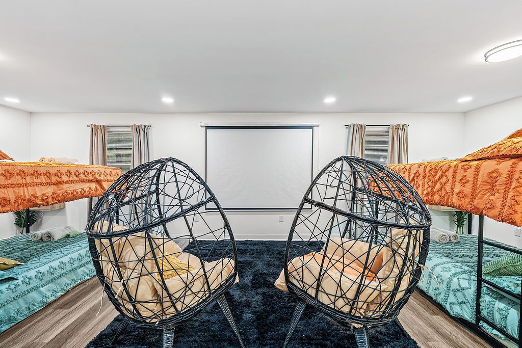 Une chambre avec deux lits, un fauteuil noir de forme circulaire et une grande fenêtre.