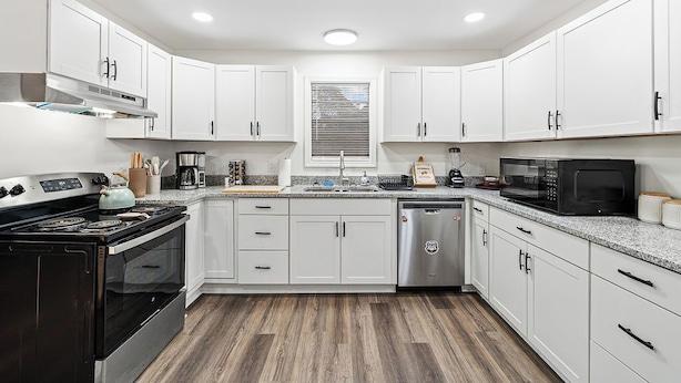 A modern kitchen with white cabinets, a stainless steel range hood, a dishwasher, and a microwave. - Spacious 5BR Athens Home | Massage Chairs & Fire Pit | Sleeps 12 | Near UGA (Athens)