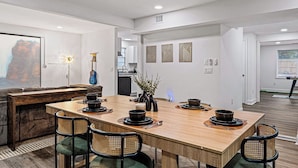 A modern dining area with a wooden table set for four, surrounded by wicker chairs. A ceiling fan and recessed lighting are visible above. - Spacious 5BR Athens Home | Massage Chairs & Fire Pit | Sleeps 12 | Near UGA (Athens)