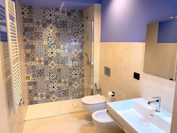 Un baño con zona de ducha que incluye una pared de mosaicos, un inodoro y un lavamanos con espejo.