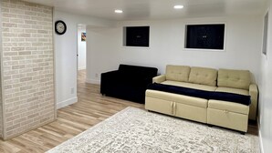 A living room with a brick accent wall, a black sofa, a beige sofa, a patterned rug, and recessed ceiling lights. - Brilliant bungalow in Midvale ski/hike, fishing, recreational activities (Midvale)